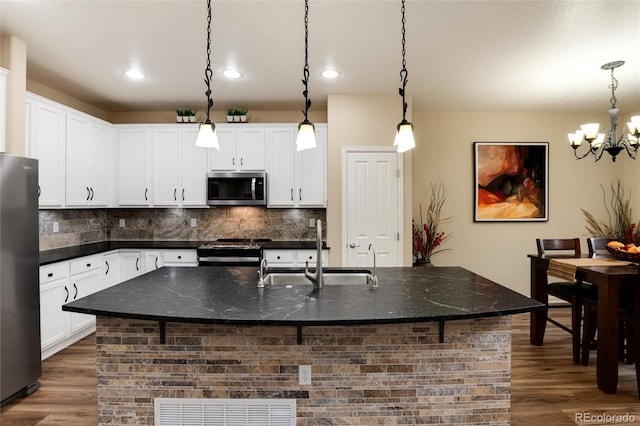 kitchen with appliances with stainless steel finishes, an island with sink, and hanging light fixtures