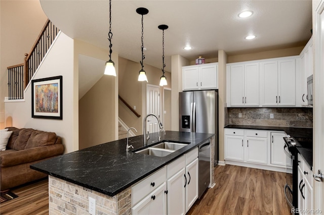 kitchen featuring sink, appliances with stainless steel finishes, white cabinetry, backsplash, and a center island with sink