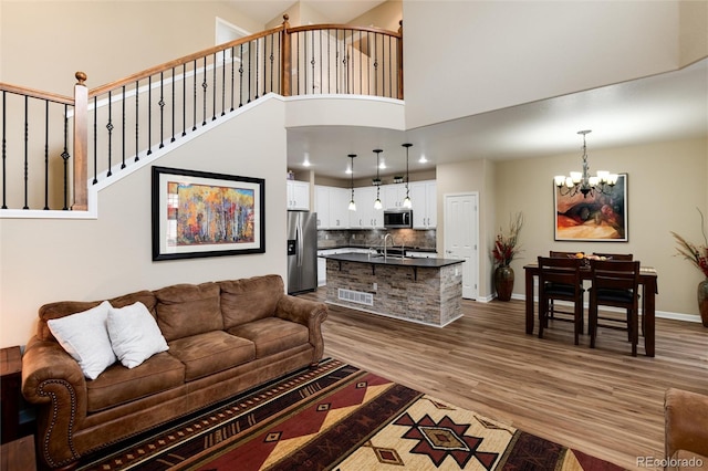 living room with a towering ceiling, sink, a chandelier, and light wood-type flooring