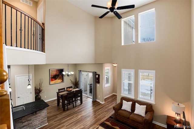 living room with a high ceiling, dark wood-type flooring, and ceiling fan with notable chandelier