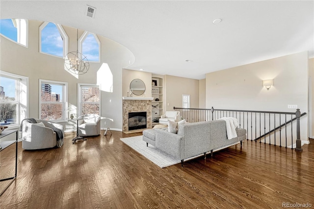 living room featuring a notable chandelier, built in shelves, dark hardwood / wood-style floors, and a tiled fireplace