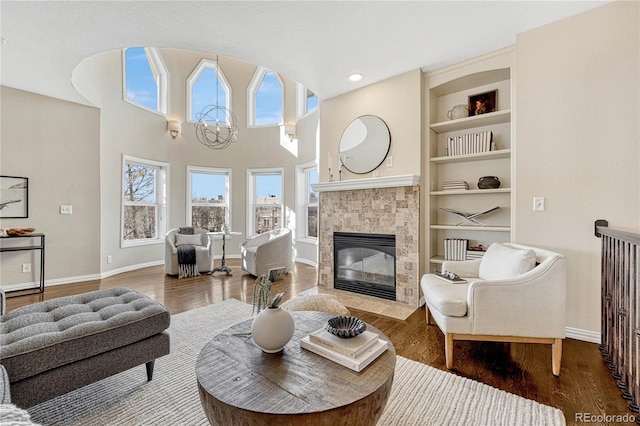 living room with a tiled fireplace, a chandelier, built in features, and hardwood / wood-style floors