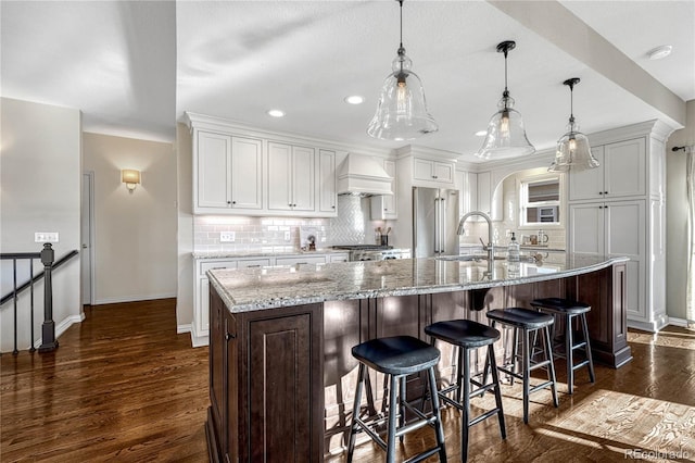 kitchen featuring decorative light fixtures, white cabinetry, premium range hood, and a large island with sink