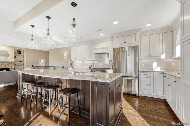 kitchen featuring a kitchen island with sink, high end fridge, white cabinets, and custom exhaust hood