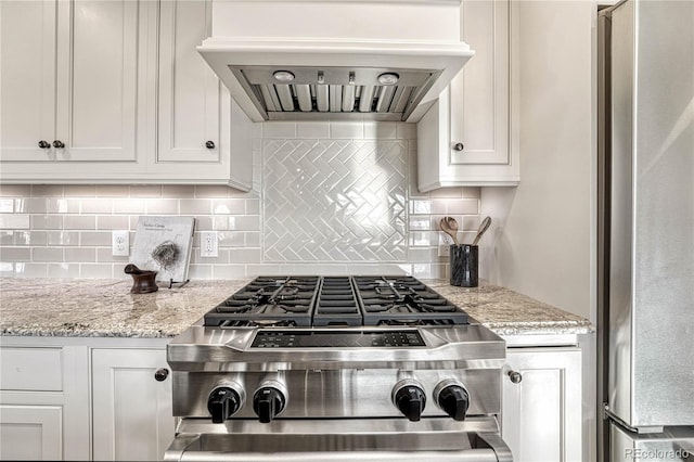 kitchen featuring custom exhaust hood, tasteful backsplash, light stone counters, white cabinetry, and stainless steel refrigerator