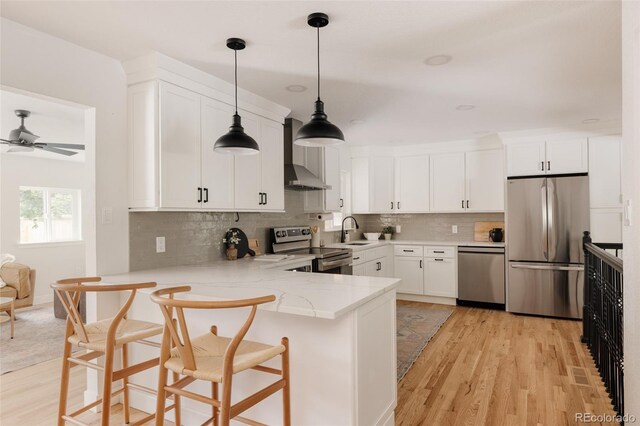 2263 Yellowstone St, Golden, CO 80401 - kitchen with appliances with stainless steel finishes, wall chimney range hood, a peninsula, light stone countertops, and light wood-type flooring