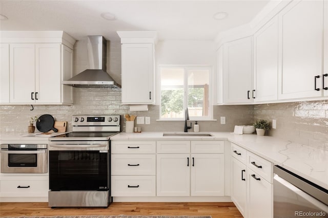 2263 Yellowstone St, Golden, CO 80401 - kitchen featuring wall chimney range hood, appliances with stainless steel finishes, white cabinets, tasteful backsplash, and light wood-type flooring