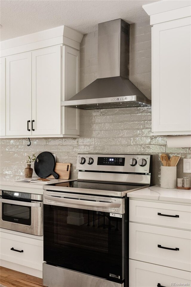 2263 Yellowstone St, Golden, CO 80401 - kitchen featuring appliances with stainless steel finishes, wall chimney exhaust hood, tasteful backsplash, and white cabinets