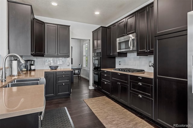 kitchen with dark wood-type flooring, sink, decorative backsplash, a textured ceiling, and appliances with stainless steel finishes