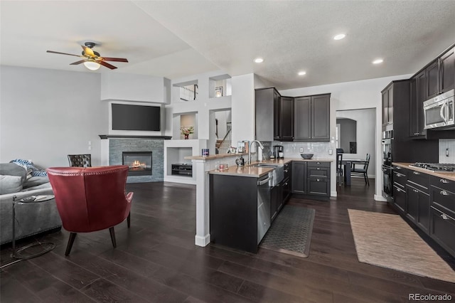 kitchen featuring stainless steel appliances, dark hardwood / wood-style flooring, kitchen peninsula, decorative backsplash, and a fireplace