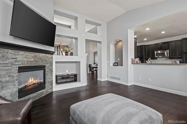 living room with lofted ceiling, dark hardwood / wood-style flooring, a stone fireplace, and built in features