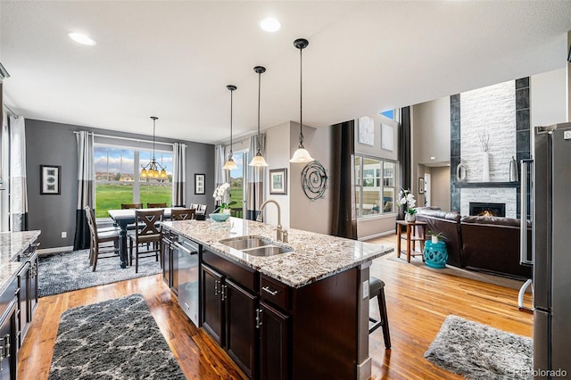 2349 Hickory Pl, Erie, CO 80516 - kitchen with appliances with stainless steel finishes, a sink, a breakfast bar area, a stone fireplace, and a healthy amount of sunlight