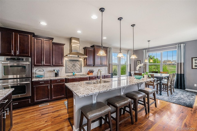 2349 Hickory Pl, Erie, CO 80516 - kitchen featuring decorative backsplash, wall chimney range hood, a sink, light wood finished floors, and stainless steel appliances