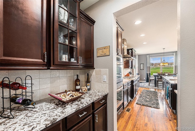 2349 Hickory Pl, Erie, CO 80516 - kitchen featuring dark brown cabinetry, backsplash, light stone countertops, glass insert cabinets, and light wood-style flooring