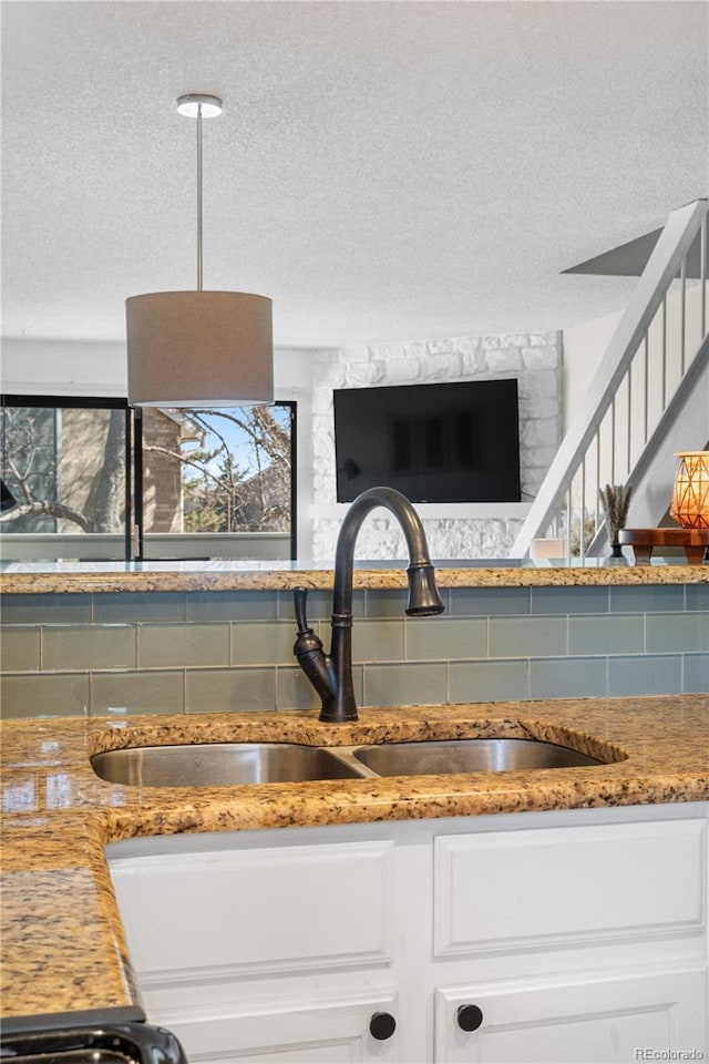 8773 W Cornell Ave Unit 10, Lakewood, CO 80227 - kitchen view of a sink, a textured ceiling, backsplash, white cabinets, and light stone countertops