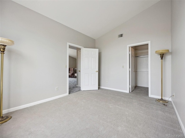 unfurnished bedroom featuring carpet floors, baseboards, a walk in closet, and high vaulted ceiling