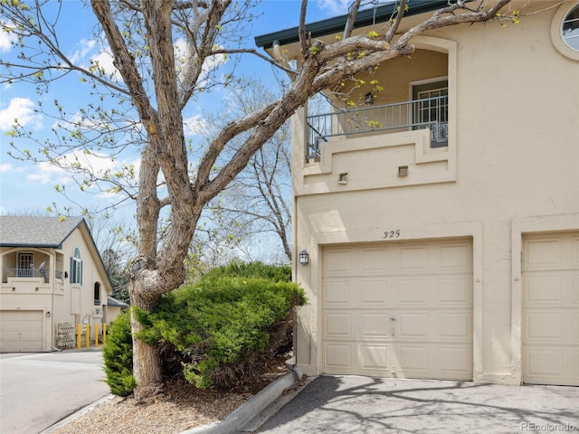 view of home's exterior featuring a balcony, stucco siding, an attached garage, and driveway
