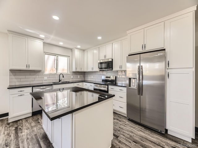 kitchen featuring stainless steel appliances, a sink, dark wood finished floors, dark countertops, and white cabinetry