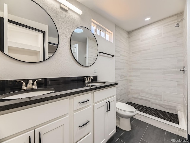 bathroom featuring a tile shower, toilet, double vanity, and tile patterned flooring