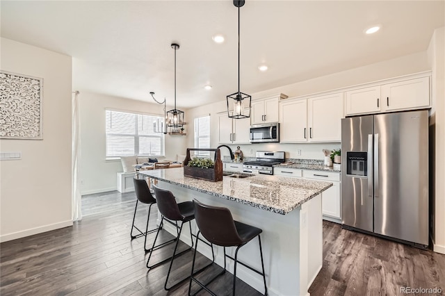 kitchen with pendant lighting, sink, white cabinets, stainless steel appliances, and a center island with sink