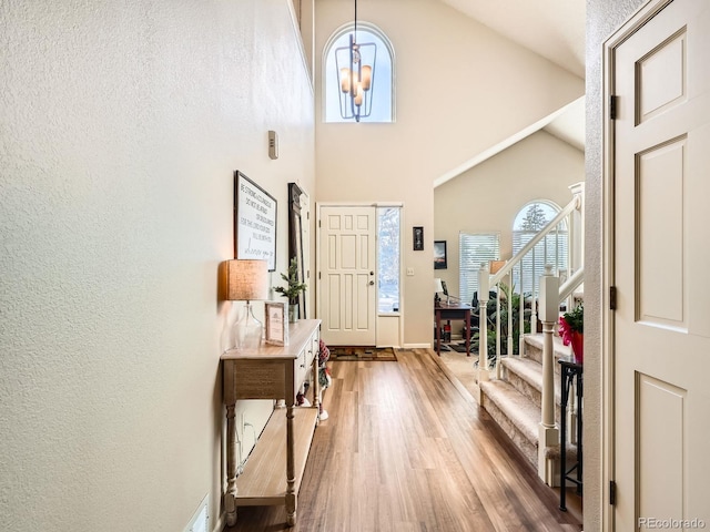 foyer entrance with hardwood / wood-style flooring, high vaulted ceiling, and an inviting chandelier