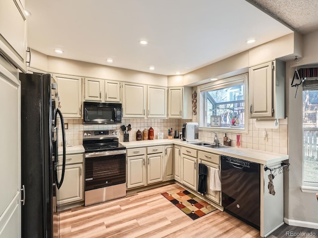 kitchen featuring black appliances, backsplash, light wood-type flooring, and sink