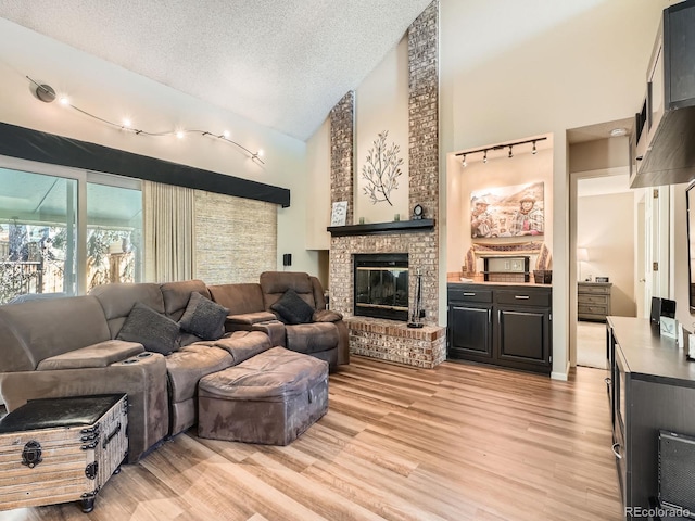 living room featuring a fireplace, a textured ceiling, high vaulted ceiling, and light hardwood / wood-style flooring