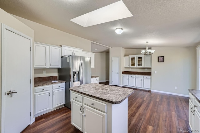 kitchen with dark wood-type flooring, stainless steel refrigerator with ice dispenser, white cabinetry, decorative light fixtures, and a kitchen island