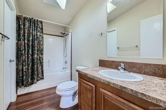 full bathroom featuring hardwood / wood-style floors, a skylight, shower / bath combination with curtain, vanity, and toilet