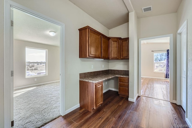 kitchen featuring dark wood-type flooring, built in desk, and vaulted ceiling