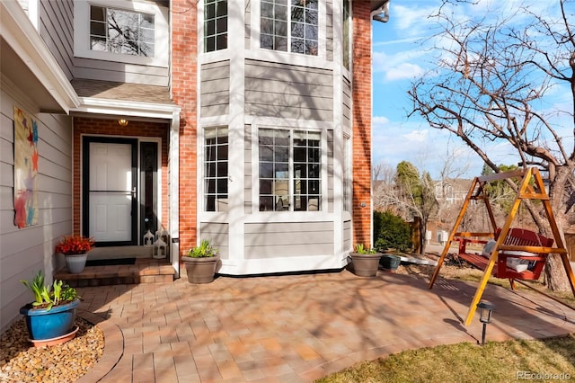 view of exterior entry with brick siding, a patio, and roof with shingles