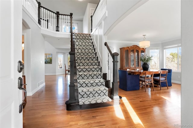 entrance foyer with light wood-type flooring, visible vents, ornamental molding, arched walkways, and baseboards