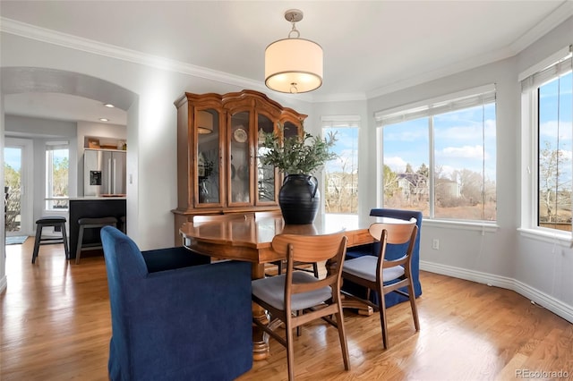 dining area featuring arched walkways, baseboards, crown molding, and light wood-style floors