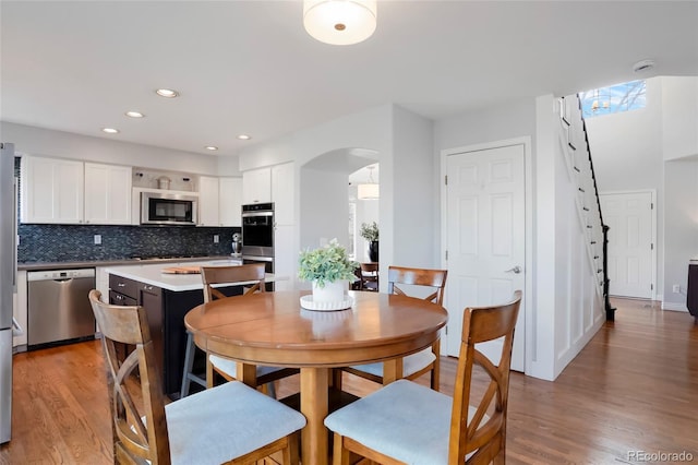 dining space with recessed lighting, arched walkways, and light wood-style floors