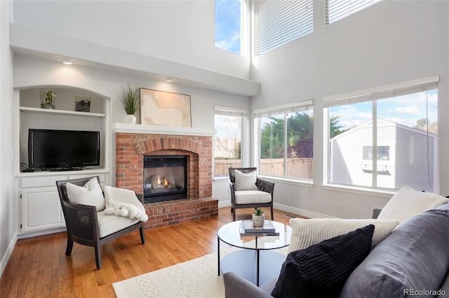 living area featuring a brick fireplace, built in features, baseboards, and light wood-type flooring