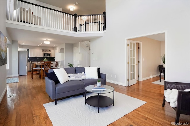 living area with stairway, baseboards, light wood-type flooring, and a towering ceiling