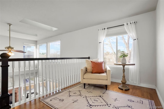 sitting room with ceiling fan, a skylight, baseboards, and wood finished floors