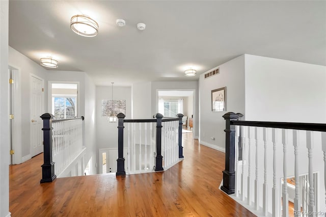 hallway featuring an upstairs landing, visible vents, a healthy amount of sunlight, and wood finished floors