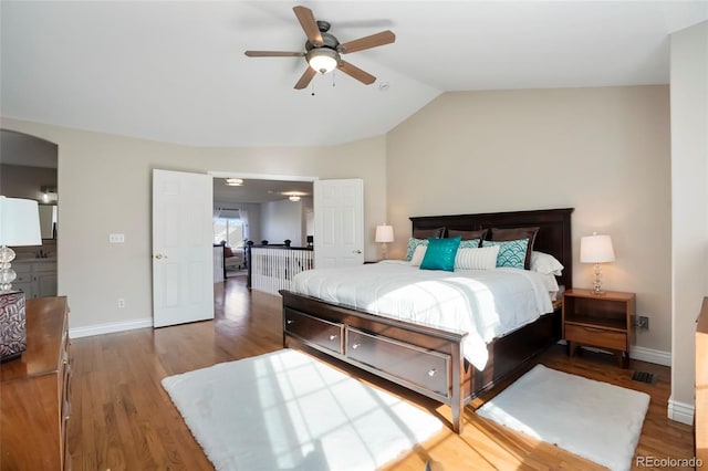 bedroom featuring wood finished floors, baseboards, lofted ceiling, arched walkways, and ceiling fan