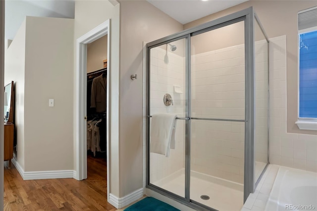 bathroom featuring a shower stall, a walk in closet, baseboards, a washtub, and wood finished floors