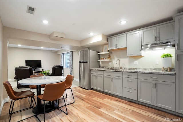 kitchen featuring gray cabinetry, under cabinet range hood, light wood-type flooring, recessed lighting, and freestanding refrigerator