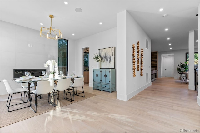 dining space with light wood-type flooring, an inviting chandelier, and a large fireplace