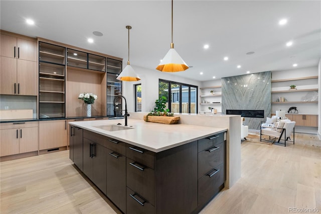 kitchen with pendant lighting, dark brown cabinets, a high end fireplace, a kitchen island with sink, and sink