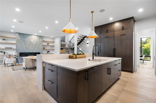 kitchen featuring a large island with sink, a fireplace, pendant lighting, light hardwood / wood-style flooring, and sink