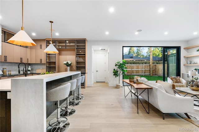 kitchen featuring tasteful backsplash, light hardwood / wood-style flooring, a kitchen breakfast bar, decorative light fixtures, and light brown cabinetry