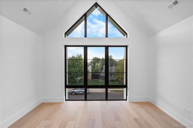 spare room featuring light hardwood / wood-style flooring, a wealth of natural light, and high vaulted ceiling