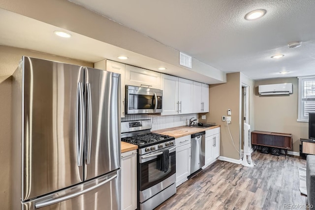 kitchen featuring appliances with stainless steel finishes, white cabinetry, wood counters, and a wall mounted AC