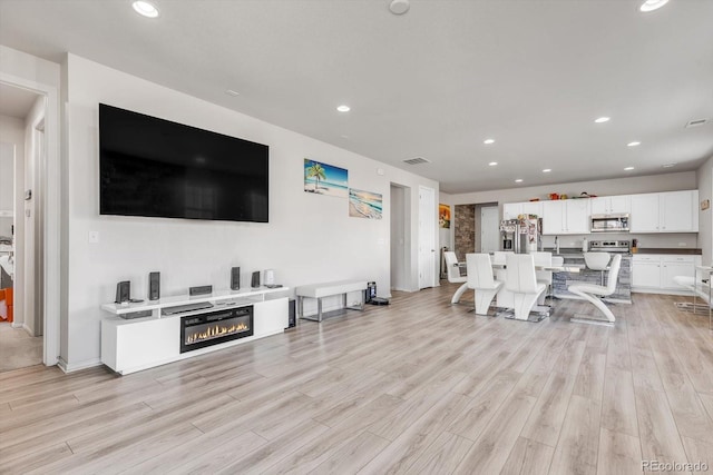 living room with light wood finished floors, recessed lighting, and a glass covered fireplace