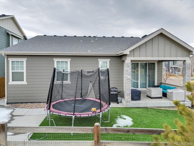 rear view of house featuring a patio, roof with shingles, a trampoline, outdoor lounge area, and board and batten siding