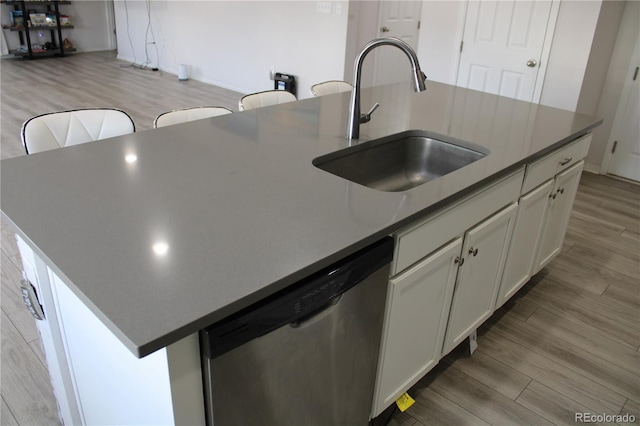 kitchen featuring light wood-type flooring, an island with sink, stainless steel dishwasher, white cabinets, and a sink